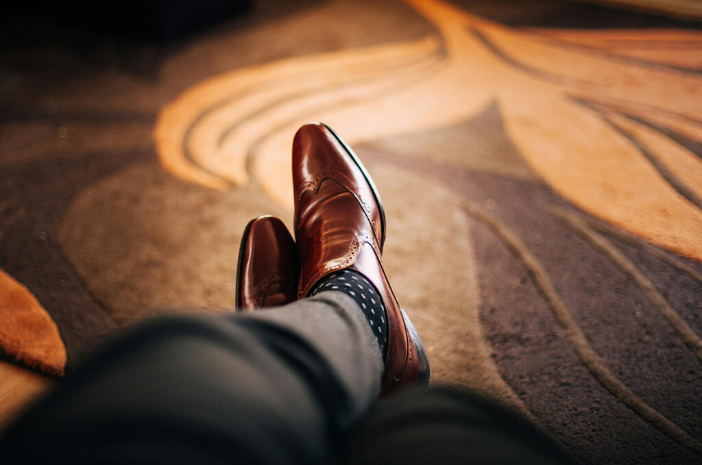 Braune Lederschuhe auf elegantem Teppich, Beine ausgestreckt. Moderne, stilvolle Szene.