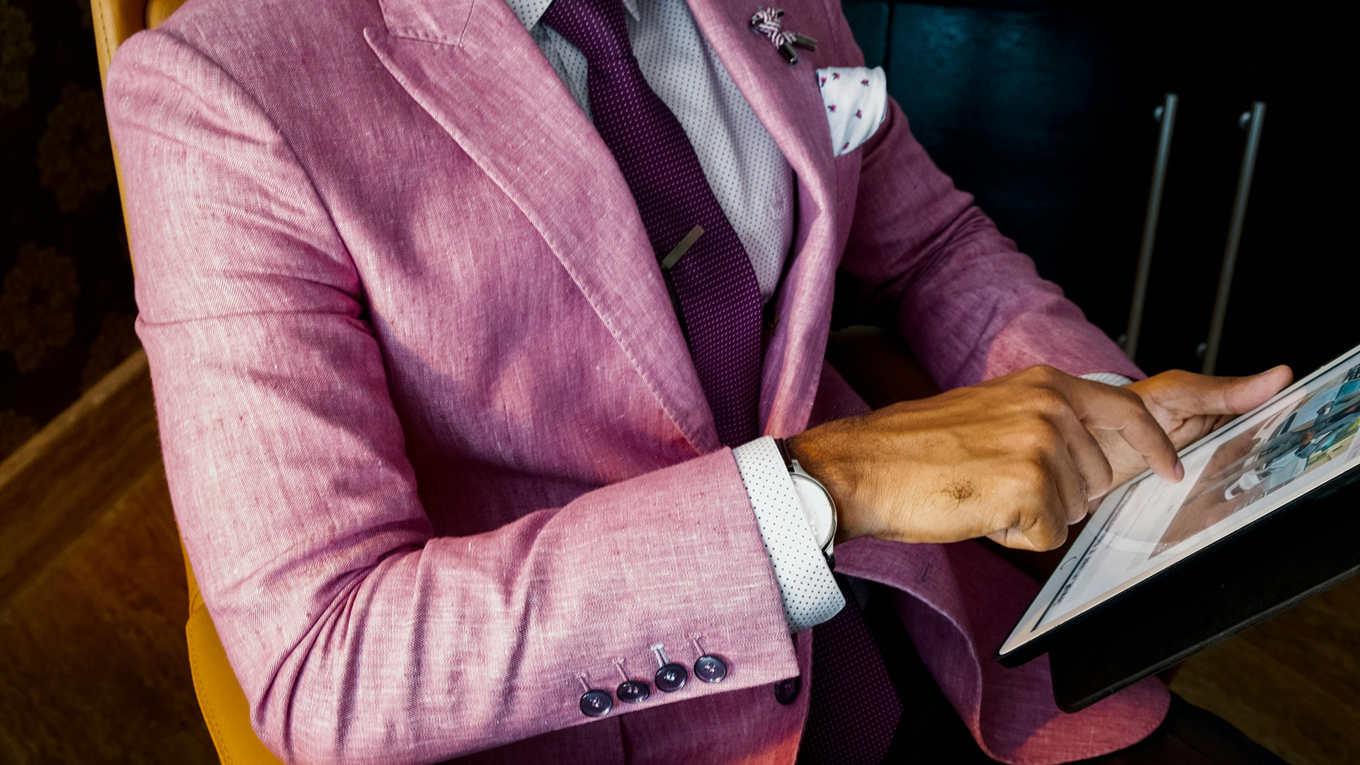 Eine Person trägt einen rosa Anzug, zeigt ernst auf ein Tablet.